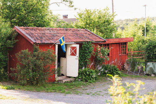 Wooden Red Cabin with Swedish Flag in Countryside Greenery
