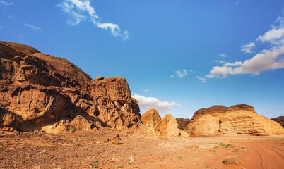 Fototapeta premium Red orange sandstone rocks formations in Wadi Rum desert, vehicle tire prints in sand road near