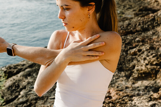 Woman performing arm stretches near a rocky beach