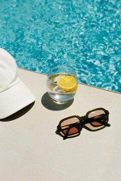Conceptual image of a cap, sunglasses and a lemon drink beside a pool