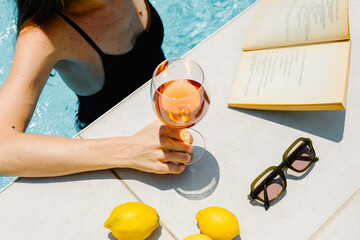 Anonymous woman reading a book and sipping wine while enjoying a pool