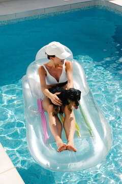 Young lady in a bikini lounging on a pool float with her pet