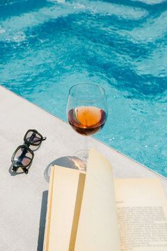 Sunglasses, a glass of wine and a book placed next to a pool