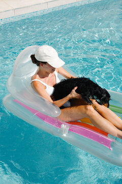 A woman relaxes on a float in a pool with her pet dog 