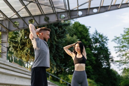 Athletic couple making stretching exercise for arms in sun rays