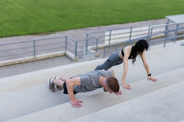 Physically fit couple doing push-ups on stairs near football field