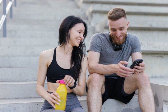 Two fitness enthusiasts sitting on stadium stairs and looking at photo