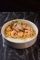 Enjoy a bowl of tasty pasta with shrimp and crispy bacon, garnished with fresh herbs