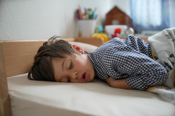 Child sleeping peacefully on bed in a cozy room, wearing a checkered shirt and surrounded by colorful toys and decor, highlighting the serenity and innocence of childhood rest