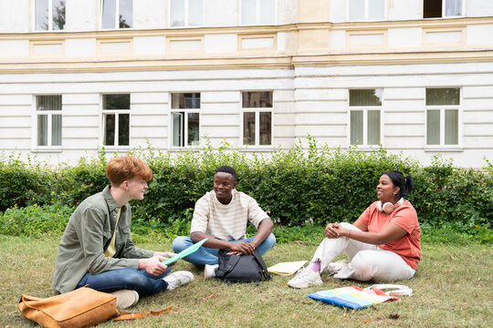 College students sitting on grass discussing test papers.