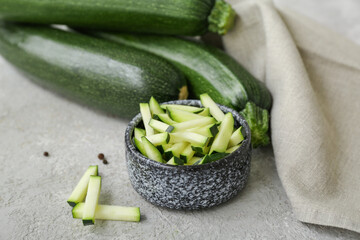 Fresh green zucchini and bowl with slices on grey background
