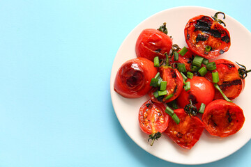 Plate with tasty grilled tomatoes and green onion on blue background