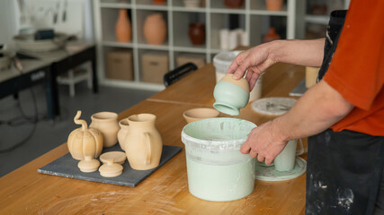 Close-up of a potter's hands glazing a pottery piece. 