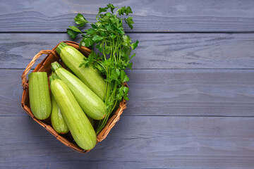 Wicker basket with many fresh green zucchini and parsley on blue wooden background