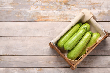 Box with fresh green zucchini on grey wooden background