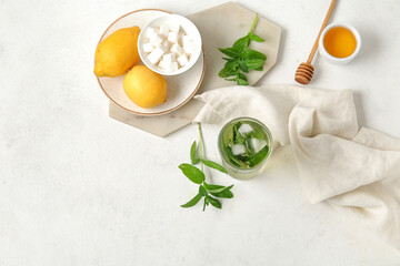 Glass of fresh icy mint tea with lemons, honey and sugar cubes on white background