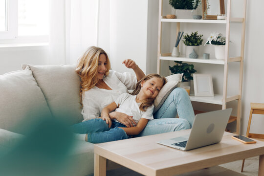 Mother and daughter bonding on couch with laptop and book in cozy living room