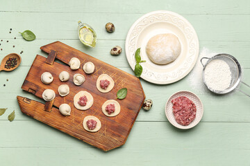 Board with uncooked dumplings and ingredients on green wooden background