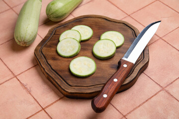 Wooden board with slices of fresh zucchini on beige tile background