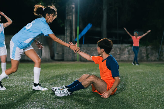 Fototapeta Non binary soccer player helping another player get up.