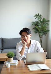 A man looking tired while working on a laptop at home, representing remote work fatigue, contemplation, and the challenges of maintaining focus in a home office.

