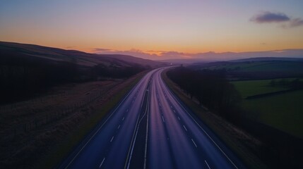 Fototapeta premium A panoramic view of a rural motorway at dusk, with gentle hills and farmland on either side, and the sky transitioning into shades of orange and purple.