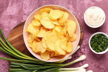 Bowls of tasty sour cream with sliced green onion and potato chips on purple background