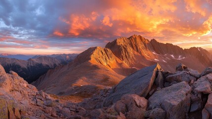 Naklejka premium A panoramic view of the sun rising above a rugged mountain peak, with vibrant orange and pink hues painting the sky and the rugged terrain bathed in the warm morning light.
