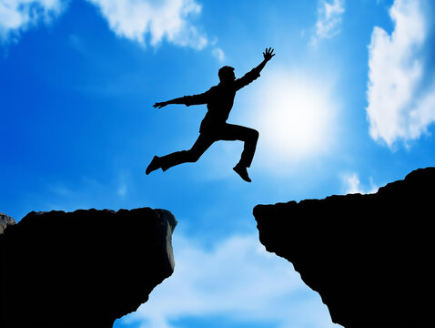 Silhouette of a man leaping across a gap between two cliffs against a bright blue sky with scattered clouds, symbolizing challenge, courage, and determination
