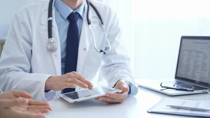 Doctor and a patient. The physician, wearing a white medical coat over a blue shirt and tie, is using tablet computer during a consultation in the clinic. Medicine
