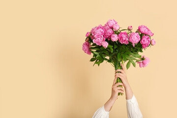 Female hands with bouquet of pink peonies on beige background