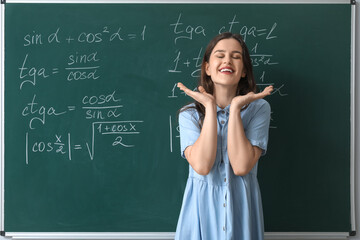 Happy female Math teacher near chalkboard in classroom