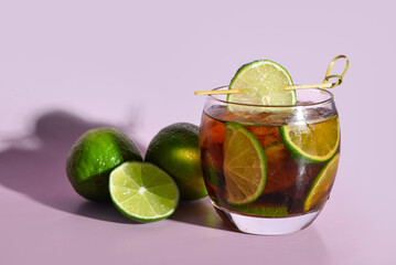 Glass of cold Cuba Libre cocktail on lilac background