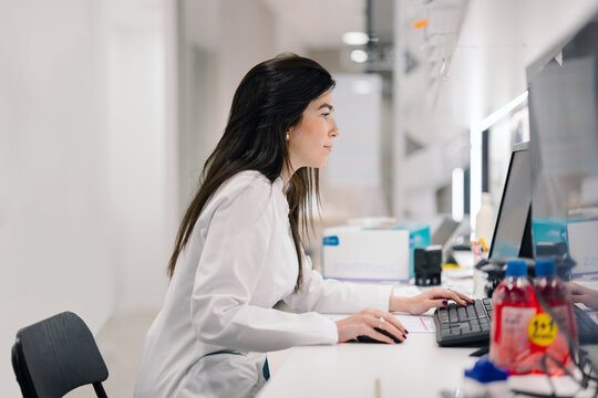 Pharmacist focused on work at computer in modern pharmacy workplace