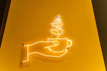 An illuminated neon sign depicts a hand gracefully holding a cup of coffee