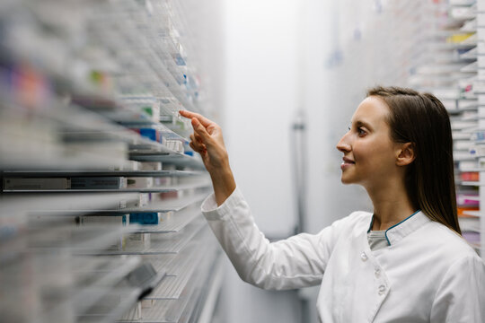 Pharmacist organizing medicine on shelf in modern pharmacy - Powered by Adobe