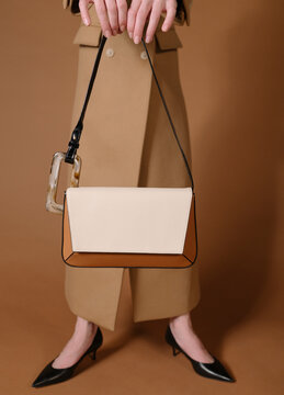 Stylish Woman Holding A Chic Handbag Against Brown Background