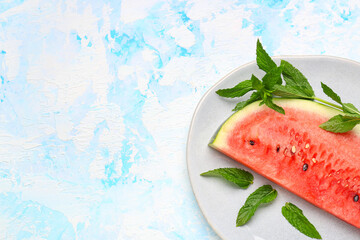 Plate with piece of fresh watermelon and mint on blue background
