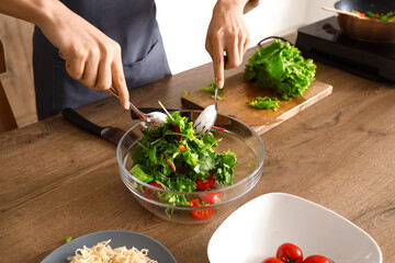 Young man making vegetable salad in kitchen, closeup