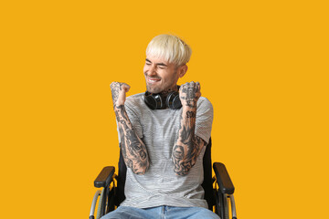 Happy young tattooed man in wheelchair on yellow background
