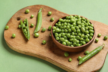 Bowl and wooden board with fresh green peas on color background