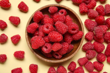 Bowl with fresh raspberries on yellow background