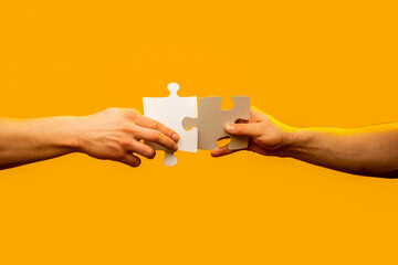 Close up, hands holding trying to connect couple jigsaw puzzle pieces isolated on yellow wall background. Association, connection concept. Men holding and putting a piece of jigsaw puzzle together