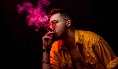 Man smoking a lit cigar, with smoke swirling around, capturing the burning. Man in glasses and smoking cigar against black background. Man with cigar and smoke
