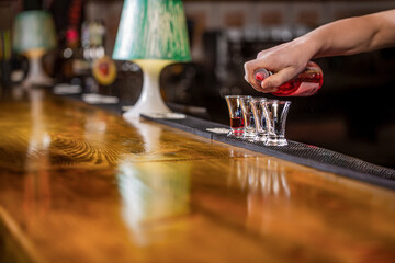 Bartender pouring strong alcoholic drink into small glasses on bar, shots. Shot glasses with liquor in the bar, colored alcohol cocktails on a party, martini, vodka. Red cocktail at the nightclub