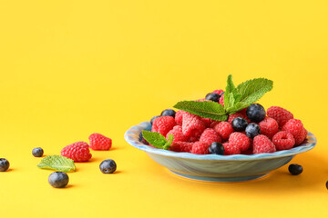 Plate with fresh raspberries and blueberries on yellow background