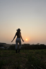 silhueta de linda vaqueira usando chapéu em pôr do sol 