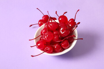 Bowl of tasty maraschino cherries on lilac background