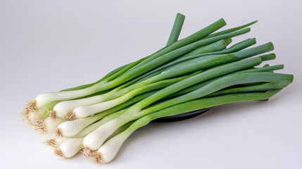 Fototapeta premium A bunch of green onions sits in a black bowl against a white backdrop.