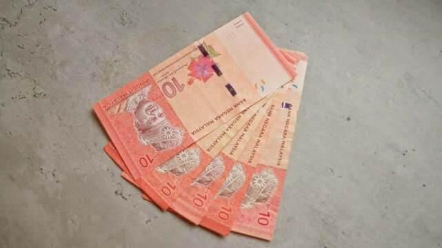 Malaysian ringgit banknotes fanned out on a concrete surface provide a detailed view of the country's currency.